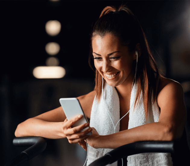 szczesliwa wysportowana kobieta korzystajaca-ze smartfona podczas cwiczen na silowni